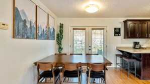 A dining area with a wooden table and chairs, a potted plant, and a kitchen area with cabinets and a countertop. - Canyon Ridge Getaway | Arcade| View | Free Massage* (Cedar Hills)