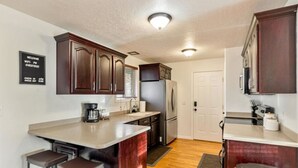 A kitchen with dark wooden cabinets, a stainless steel refrigerator, a coffee maker, and a trash can. - Canyon Ridge Getaway | Arcade| View | Free Massage* (Cedar Hills)