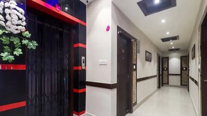 A hotel hallway with a black and red entrance, a white tiled floor, and doors leading to rooms. - The Ganga Residency (Barh)