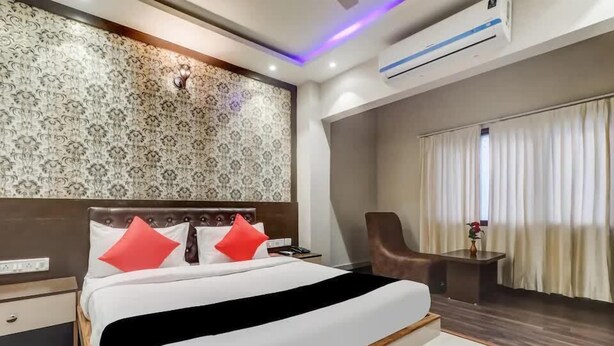A modern hotel room with a large bed, a nightstand, a chair, and a small table with a vase. - The Ganga Residency (Barh)