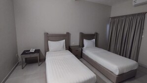 Une chambre d’hôtel avec deux lits simples, une table de chevet avec un téléphone et une fenêtre avec des rideaux.