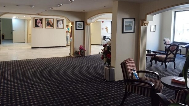 Un hall d’hôtel avec un tapis à motifs, des tableaux encadrés aux murs et un comptoir de réception.