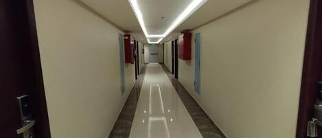 A long, narrow hallway with a shiny tiled floor and a ceiling with linear lighting.