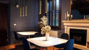 Uma sala de jantar com uma mesa branca e cadeiras azuis, um vaso com flores secas e uma lareira com velas.