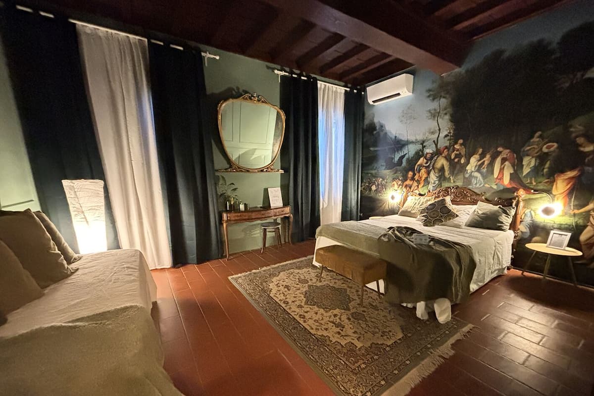 A bedroom with a large bed, a desk, a chair, a mirror, and a painting on the wall.