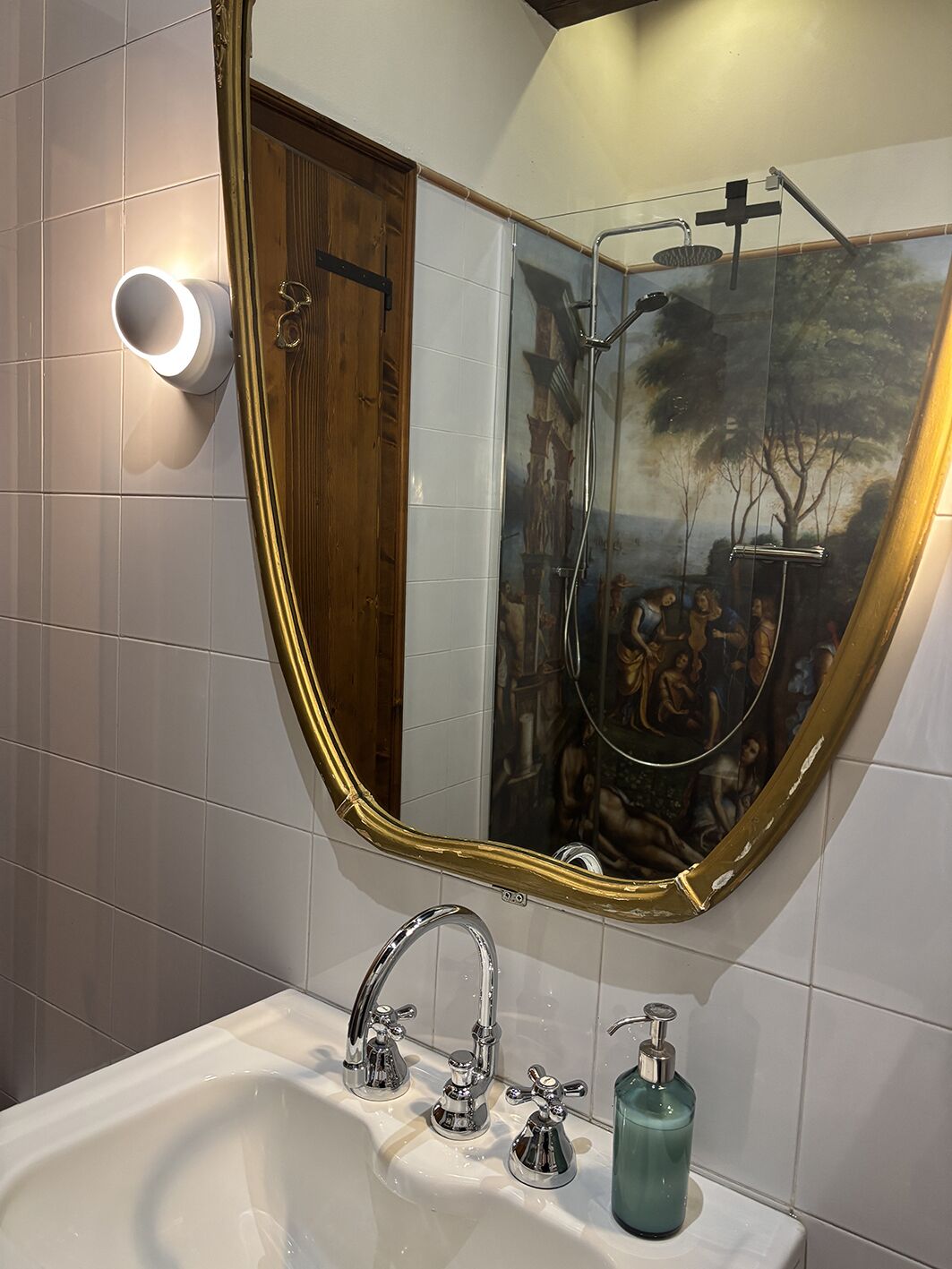 A bathroom with a large mirror, a sink with multiple faucets, and a green soap dispenser.