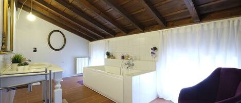 A bathroom with a bathtub, a sink, and a vanity. There is a purple chair and a round mirror on the wall.