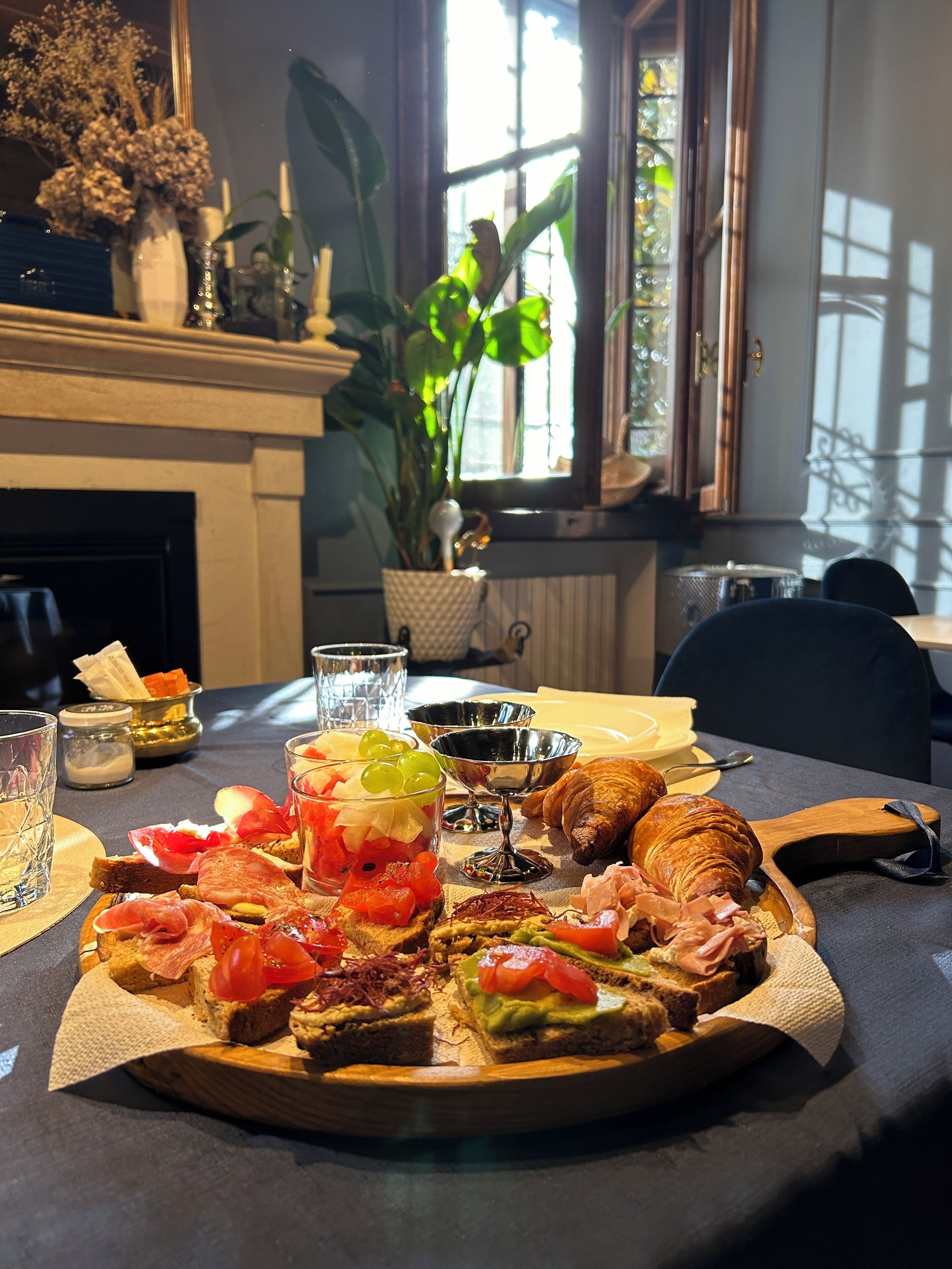 A dining table with a variety of food items, including sandwiches, croissants, and a fruit salad.