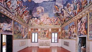 Um quarto amplo com teto alto, frescos elaborados no teto e detalhes arquitetônicos clássicos.