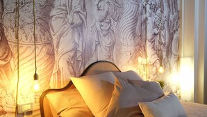 Uma cama com roupa de cama branca e várias almofadas, uma cabeceira e uma parede com um mural detalhado.