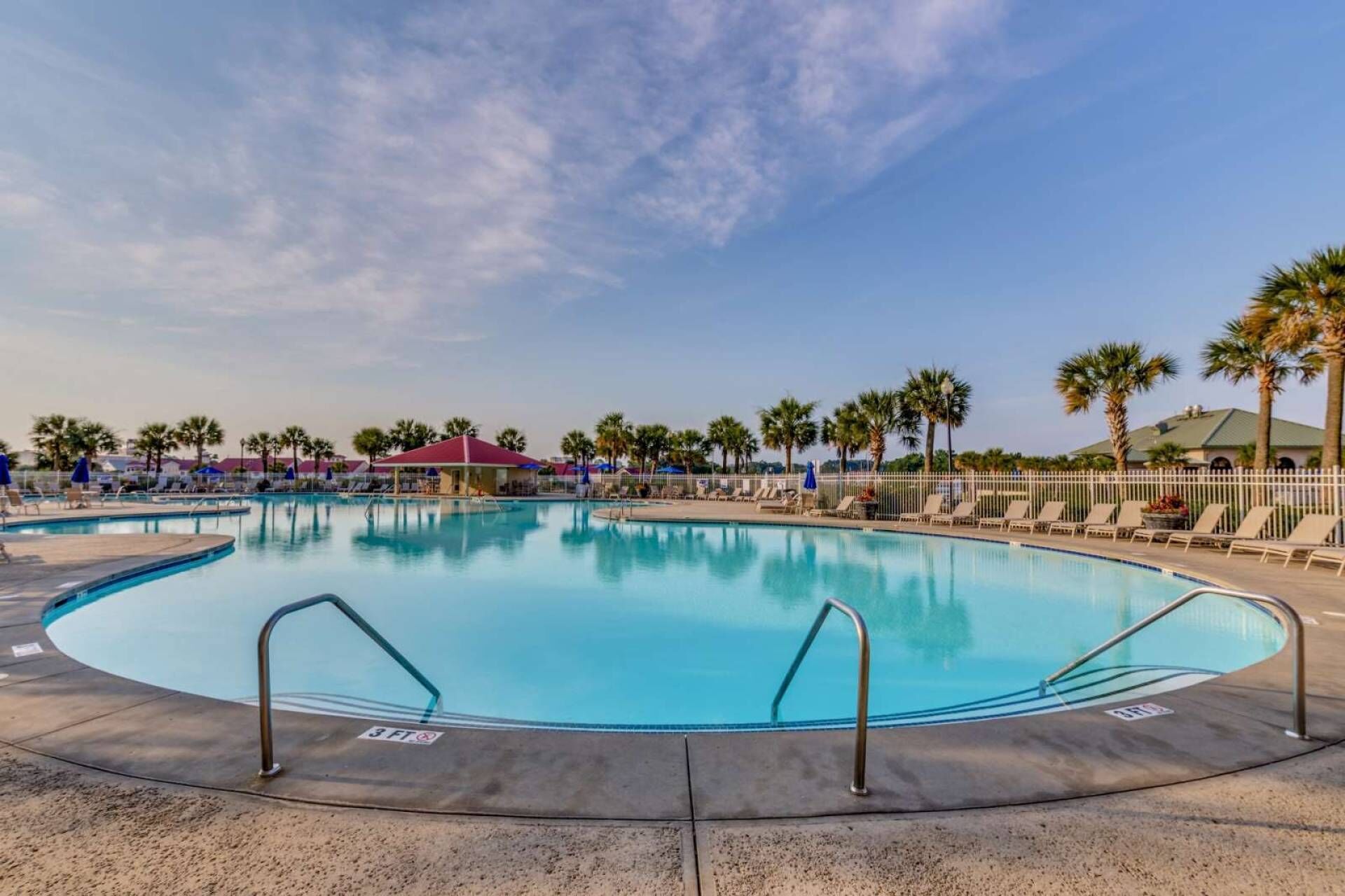A large, clear swimming pool with a 3-foot depth marker, surrounded by lounge chairs and palm trees.