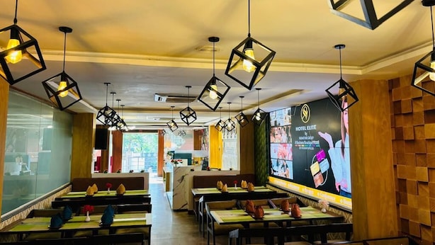 En modern restaurang med geometriska hänglampor, väggar beklädda med träpaneler och en stor digital skärm som visar information om hotellet.