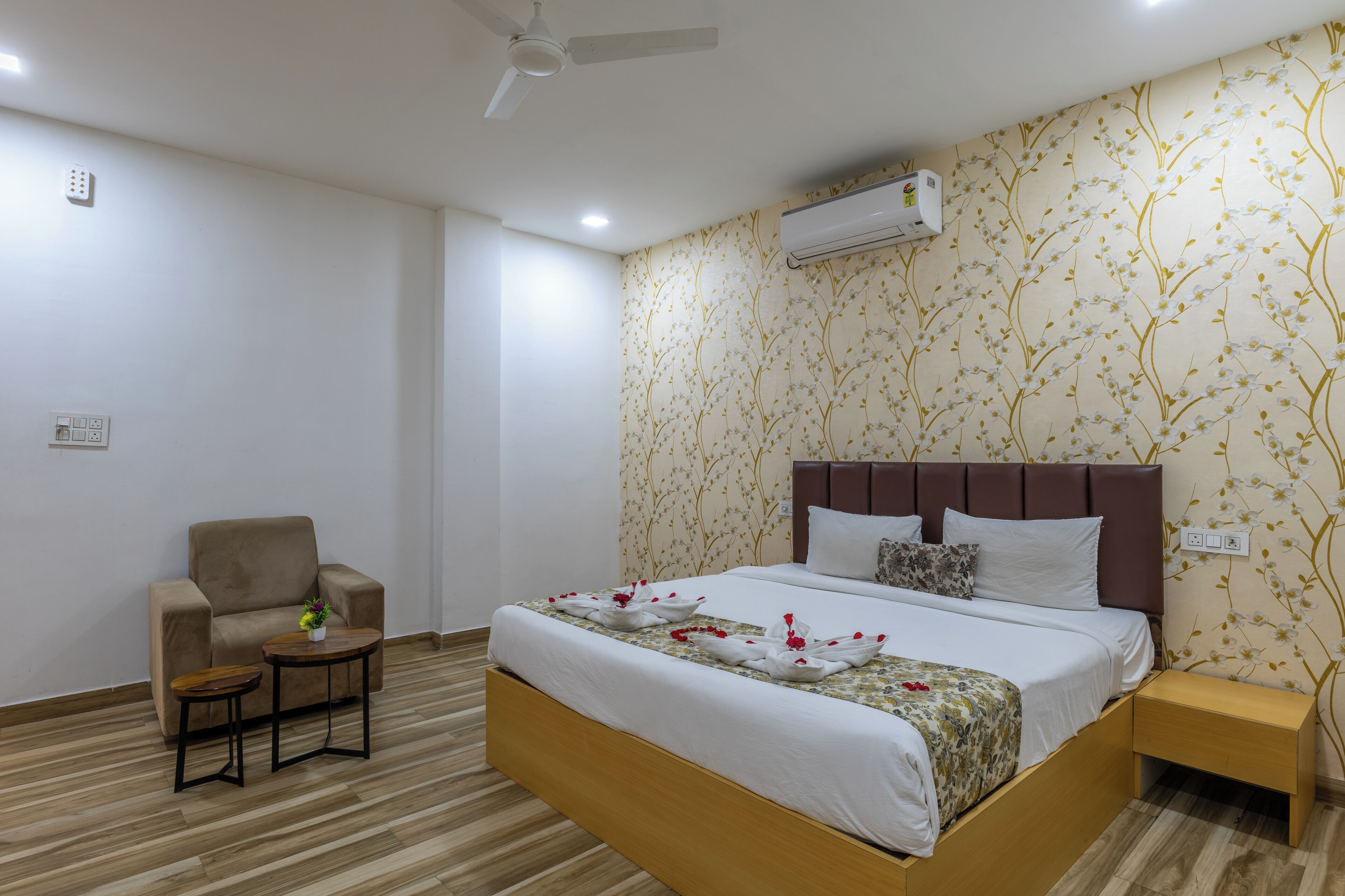 Quarto de hotel com cama, poltrona, mesinha e ar condicionado na parede.