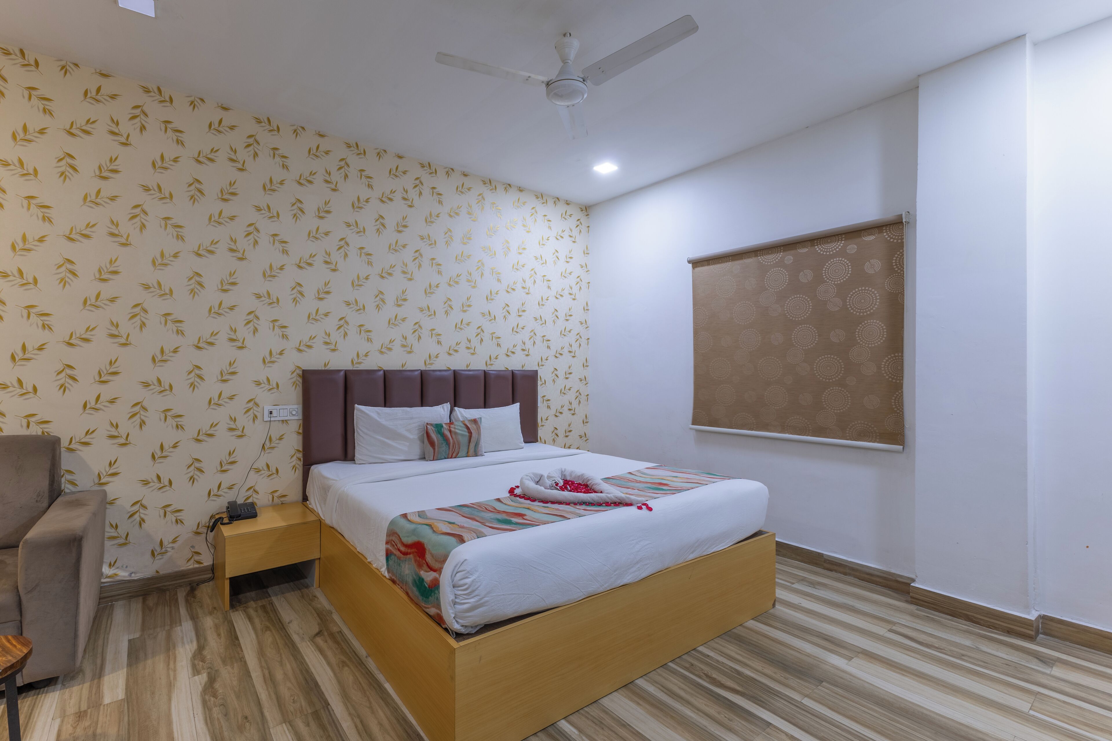 A hotel room with a bed, a chair, a nightstand, a ceiling fan, and a window with a blind.