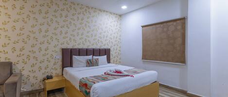 A hotel room with a bed, a chair, a nightstand, a ceiling fan, and a window with a blind.