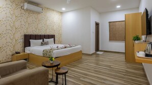 Ett hotellrum med en säng, ett skrivbord, en stol, ett litet bord, en luftkonditionering, en takfläkt och ett fönster.