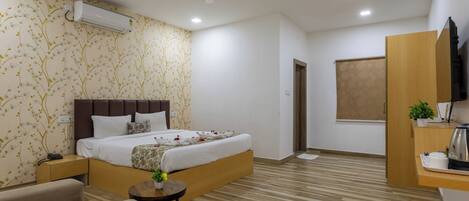 A hotel room with a bed, a desk, a chair, a small table, an air conditioner, a ceiling fan, and a window.