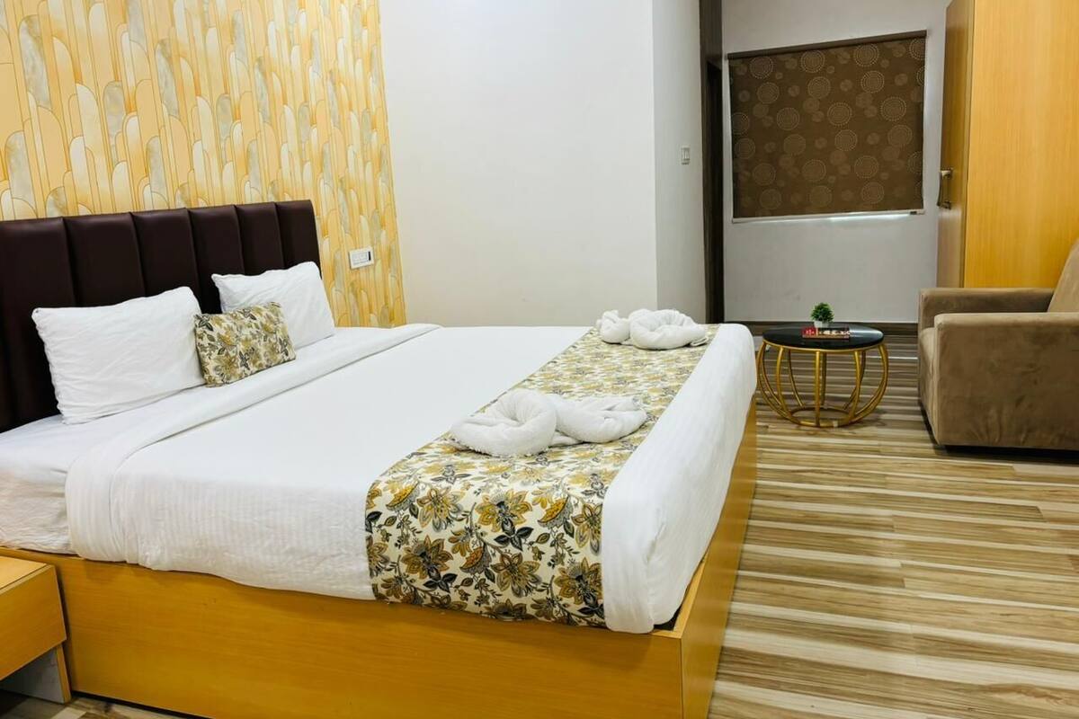 Hotellihuone, jossa on suuri sänky, puinen pääty, pieni pyöreä pöytä, jossa on kasvi, ja ruskea nojatuoli.