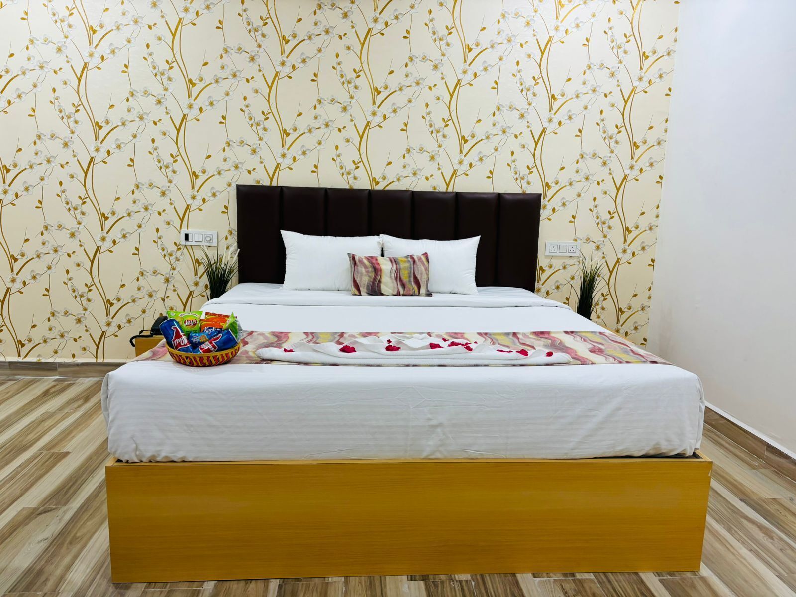 A neatly made bed with white linens and a colorful throw blanket, a dark headboard, and a wooden platform.