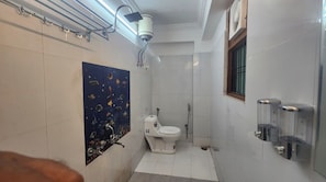 A bathroom with a toilet, shower, and a wall-mounted soap dispenser. - Sojourn Inn (Lucknow)
