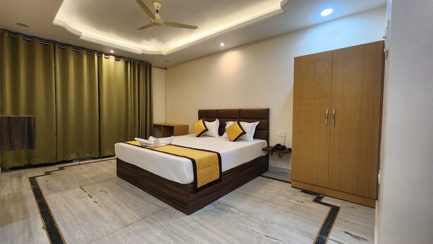 A hotel room with a large bed, a wardrobe, a bedside table, and a ceiling fan. - Sojourn Inn (Lucknow)