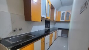A kitchen with a black countertop, white and yellow cabinets, and a stainless steel sink. - Sojourn Inn (Lucknow)