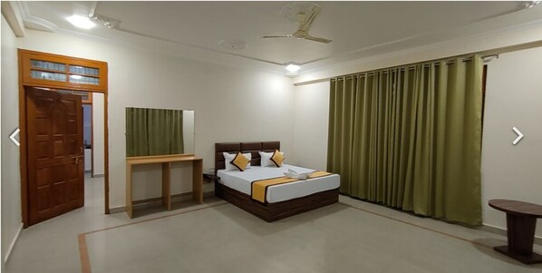 A hotel room with a bed, a desk, a ceiling fan, and curtains. - Sojourn Inn (Lucknow)