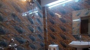 A bathroom with a marble wall, a toilet, a sink, and a ceiling-mounted light fixture. - Sojourn Inn (Lucknow)