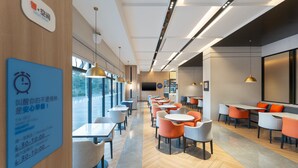 A modern cafe with tables and chairs, a large window, and a sign indicating breakfast hours. - Holiday Inn Express Guangzhou University Town by IHG (Guangzhou)