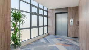 A modern elevator with a control panel, a large window with blinds, and a patterned carpet. - Holiday Inn Express Guangzhou University Town by IHG (Guangzhou)