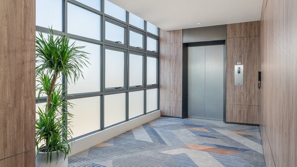 A modern elevator with a control panel, a large window with blinds, and a patterned carpet. - Holiday Inn Express Guangzhou University Town by IHG (Guangzhou)