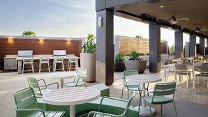 An outdoor patio area with round tables and chairs, a grill station, and potted plants.