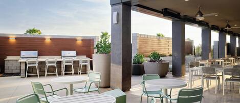 An outdoor patio area with round tables and chairs, a grill station, and potted plants.