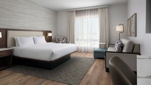 A modern hotel room with a large bed, a desk, a chair, and a sofa.