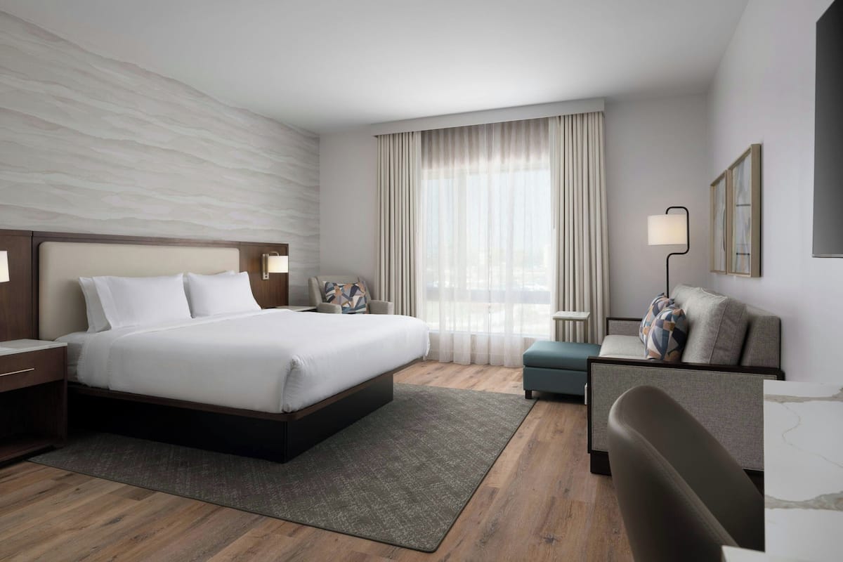 A modern hotel room with a large bed, a desk, a chair, and a sofa.