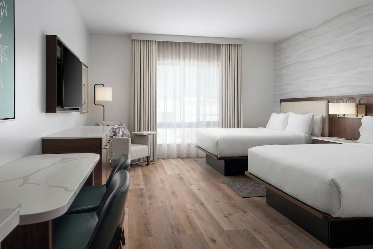 A hotel room with a bed, a desk, a chair, a TV, and a window with curtains.