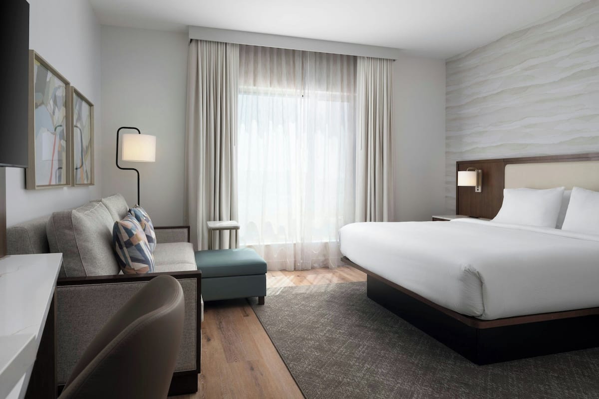 A hotel room with a bed, a sofa, a desk, and a lamp.
