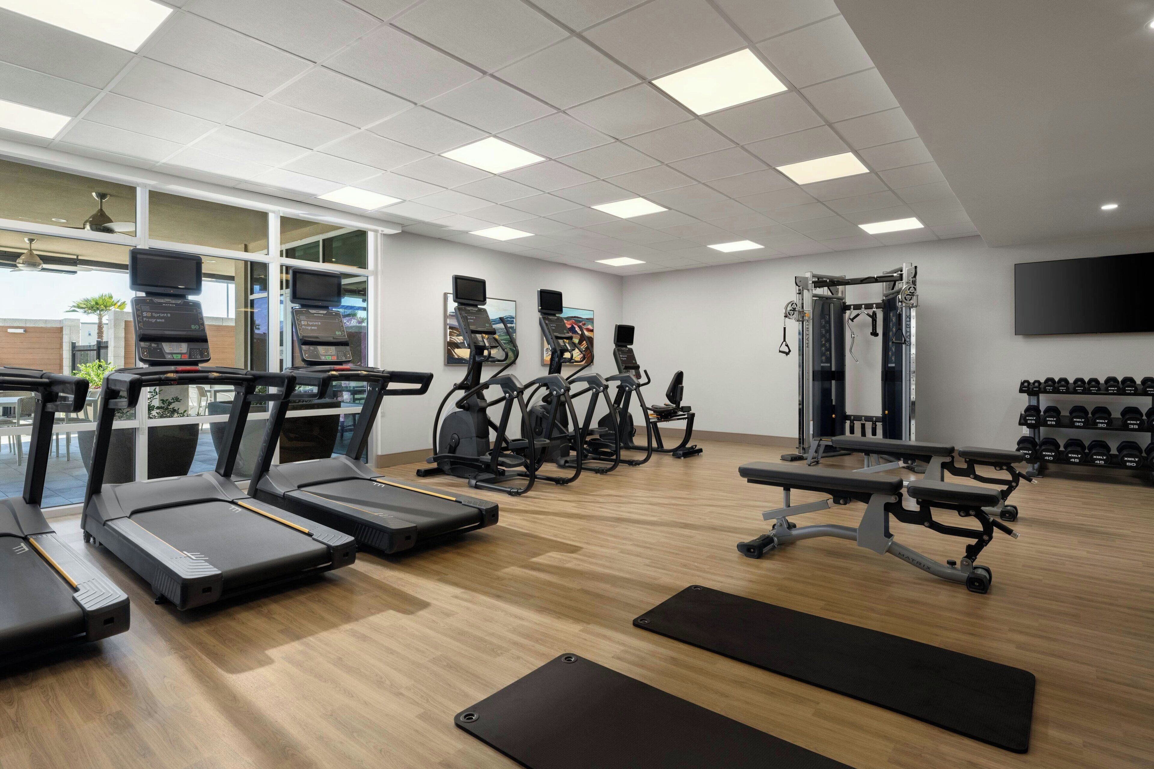 Une salle de sport équipée de tapis de course, de vélos elliptiques, d’un banc de musculation et d’un support à squats.