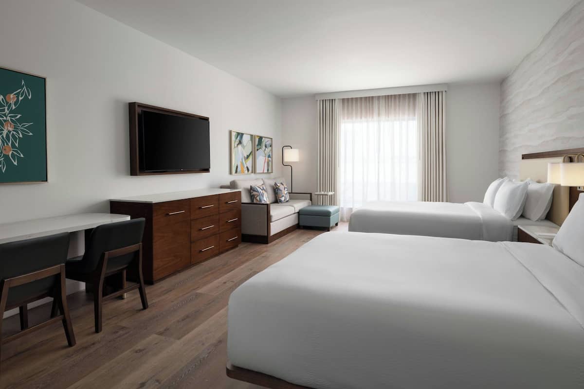 A hotel room with a bed, a desk, a chair, a TV, and a window with curtains.