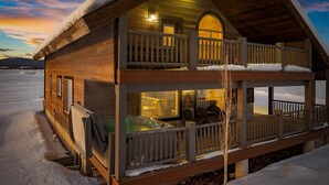 Una cabaña de madera con balcón y jacuzzi, rodeada de nieve.