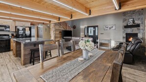 Una cocina amplia con una isla central, un comedor con mesa y sillas, una chimenea y una sala de estar con sofá y televisor.