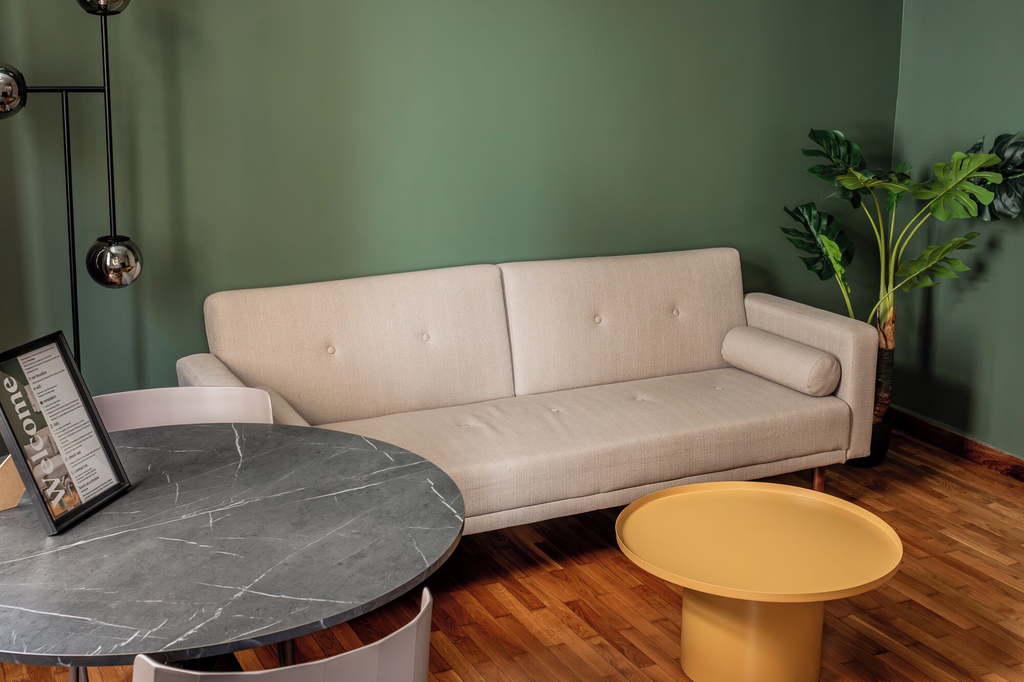 A room with a beige sofa, a round marble table, and a yellow stool.