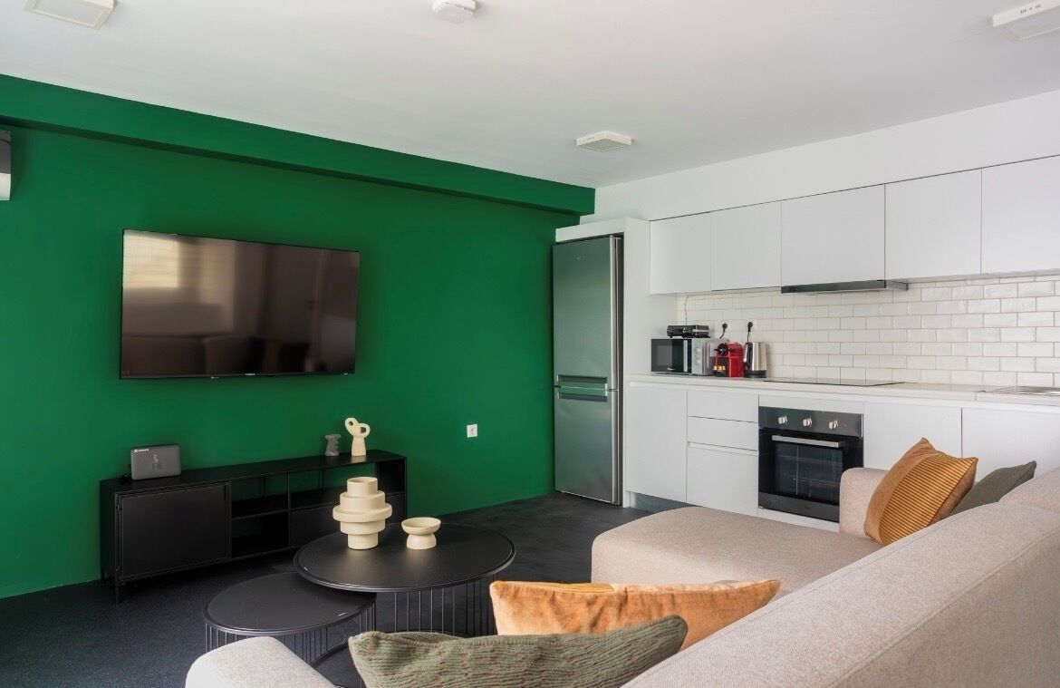 A modern living room with a green accent wall, a flat-screen TV, a black console table, and a beige sofa with cushions.