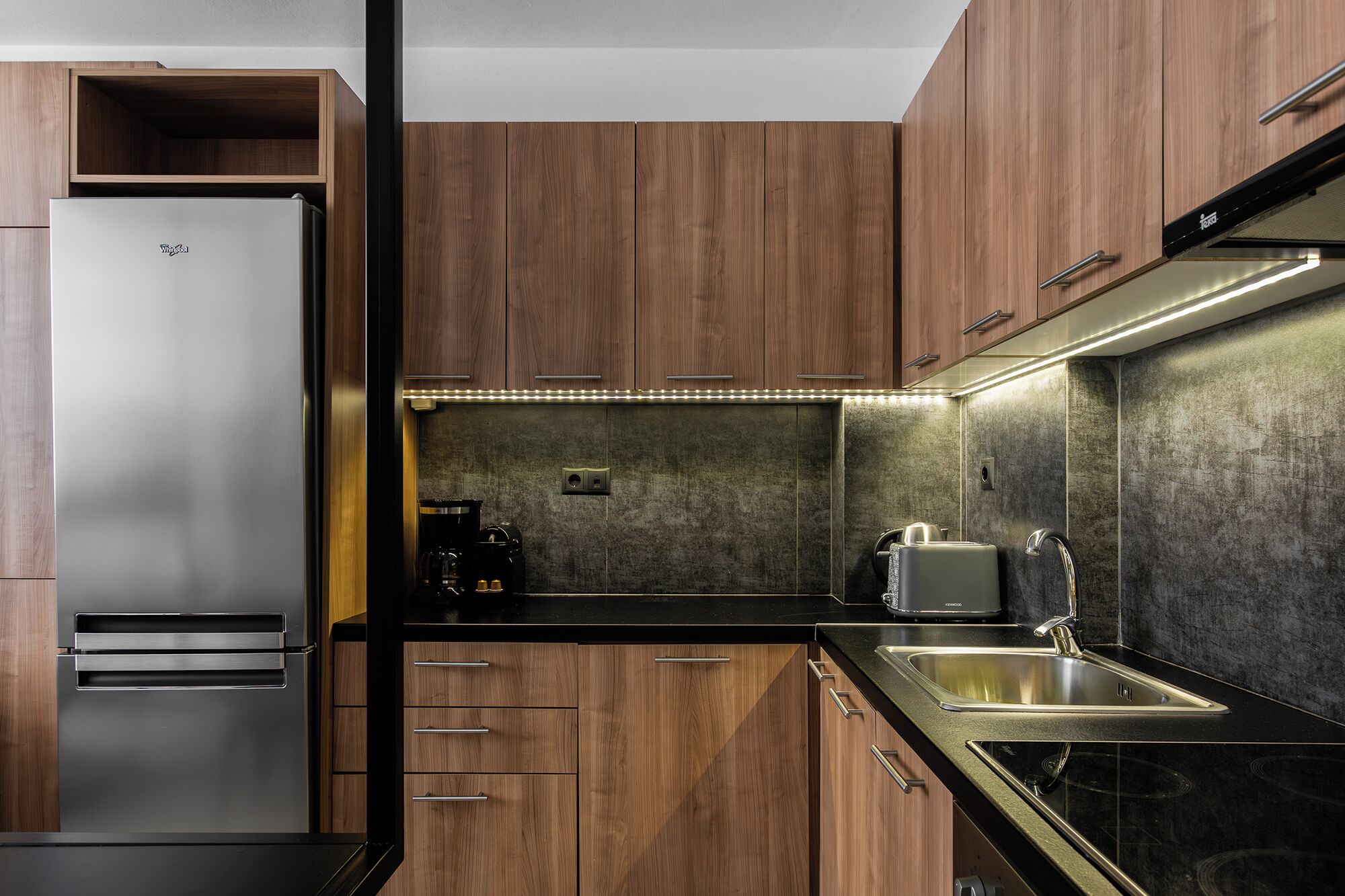 Una cocina moderna con gabinetes de madera, un refrigerador de acero inoxidable, una cafetera y un fregadero.