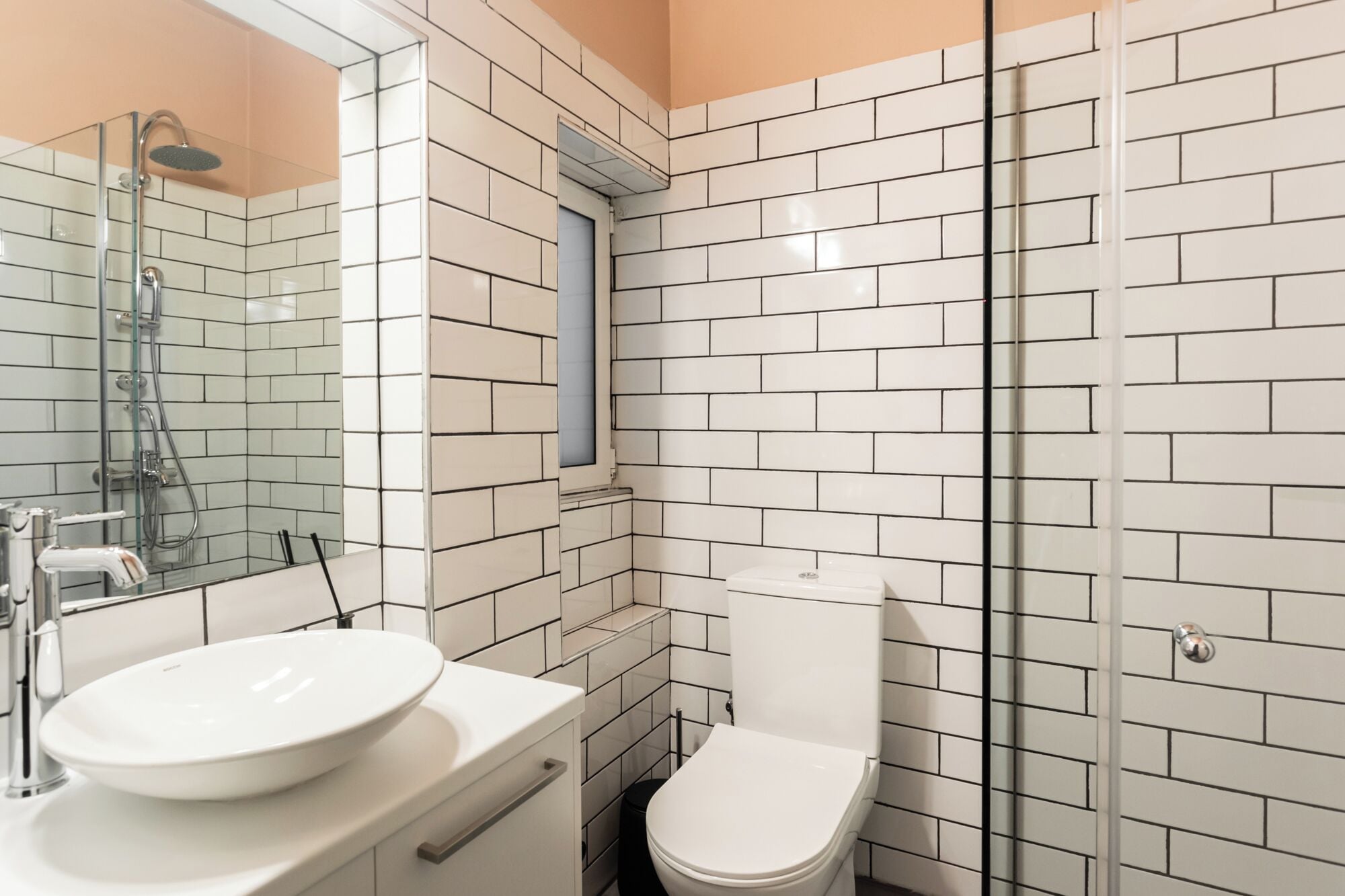 A bathroom with white subway tiles, a glass shower enclosure, a white sink, and a toilet.