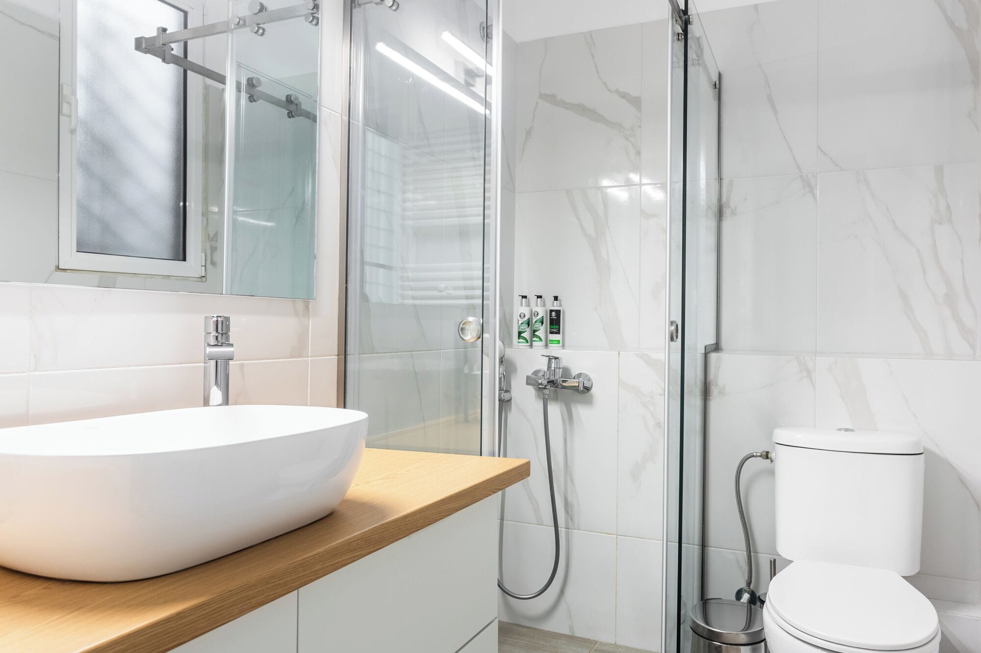 A modern bathroom with a large white sink, a glass shower enclosure, and a toilet.
