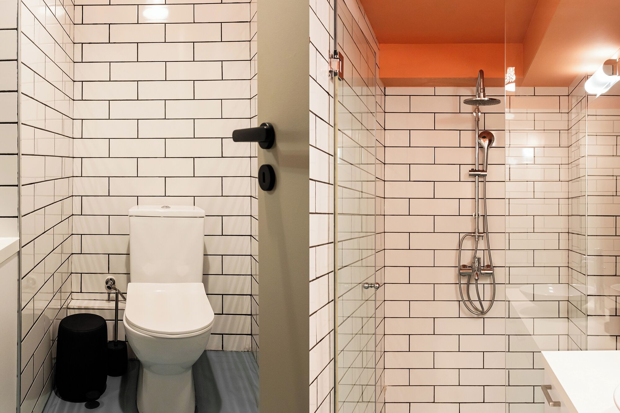 A bathroom with white subway tiles, a toilet, a black trash bin, and a glass-enclosed shower area.