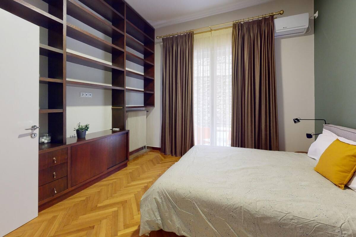 A bedroom with a bed, a wardrobe, a radiator, and a window with curtains.
