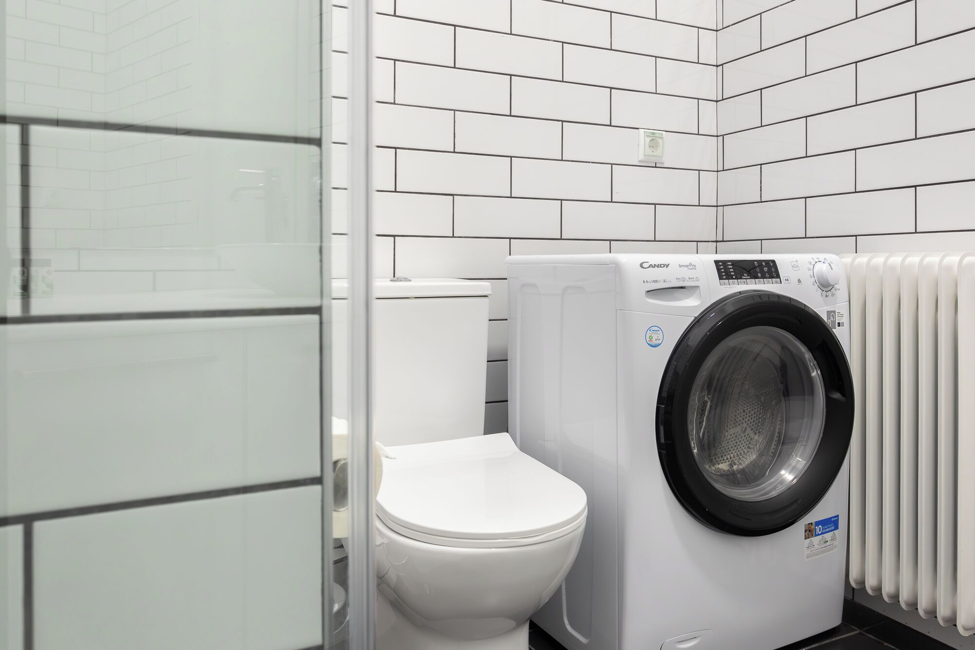 Ein kleines Badezimmer mit Toilette, einer Waschmaschine mit Frontlader und einem weißen Heizkörper.
