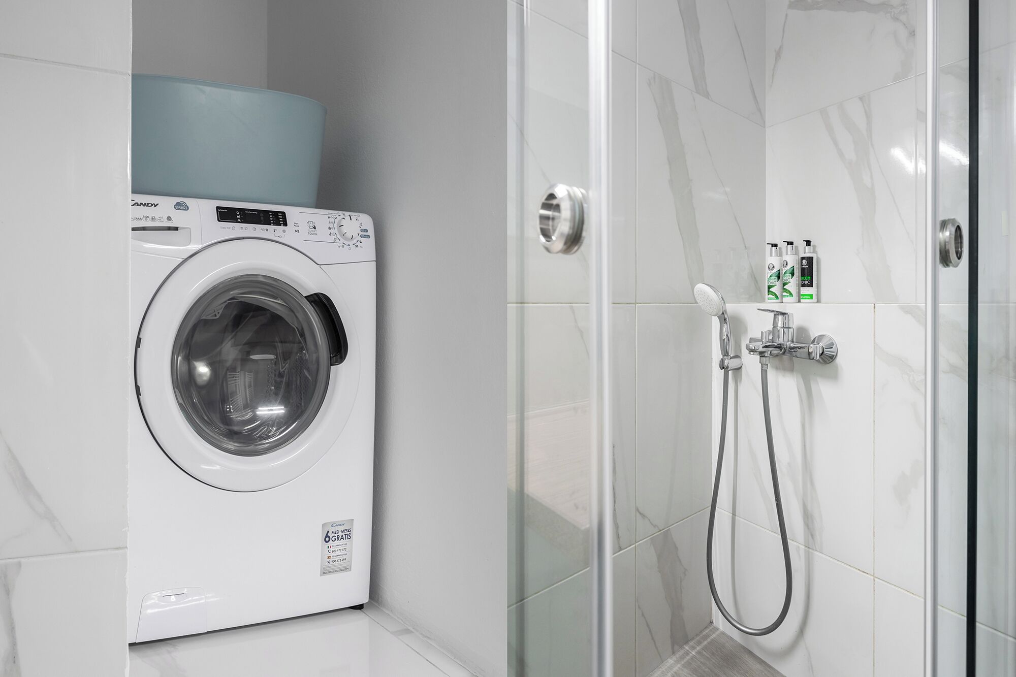 A modern bathroom with a white washing machine, a glass shower enclosure, and a hand shower.